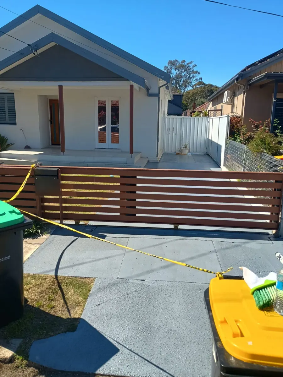 Finished grey-coated concrete driveway and path in front of a white house with a timber slat gate