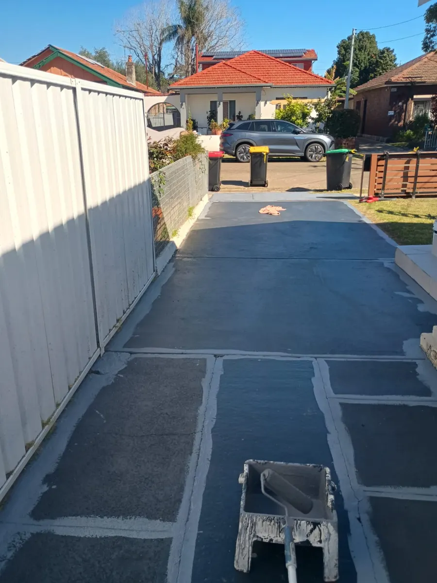Concrete driveway partway through its first coat of grey paint, roller tray in the foreground