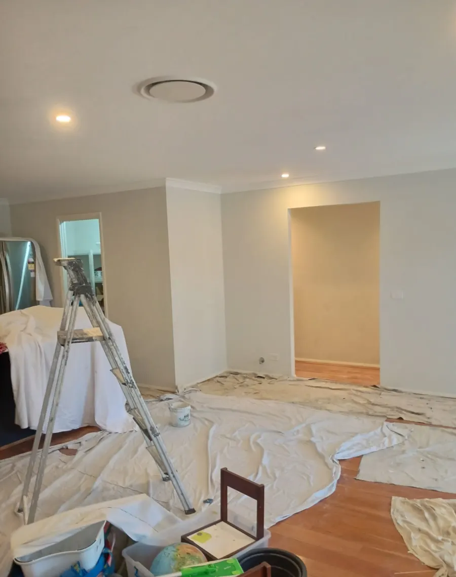 Living room mid-repaint with furniture covered and drop sheets over the floor