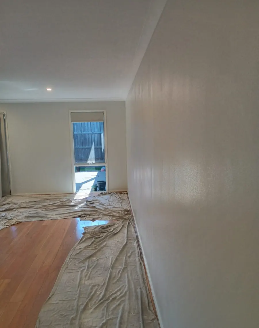 Freshly painted light grey interior wall with timber floor protected by drop sheets